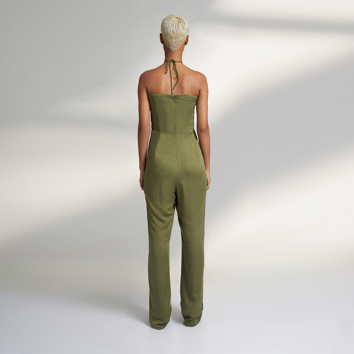 A global small size model wearing a solid olive green jumpsuit, highlighted with hand-stitched smocking on the bodice panel with a drawstring attached to the bodice to tie at the neck. inspired from the vintage window designs.