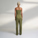 A global small size model wearing a solid olive green jumpsuit, highlighted with hand-stitched smocking on the bodice panel with a drawstring attached to the bodice to tie at the neck. inspired from the vintage window designs.