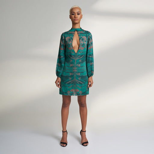 A global small size model wearing a shirt dress printed with hues of green and peach crafted in organic lotus stem silk fabric with a deep front slit neckline and gathered sleeves. the dress is printed with non toxic Gots certified inks.