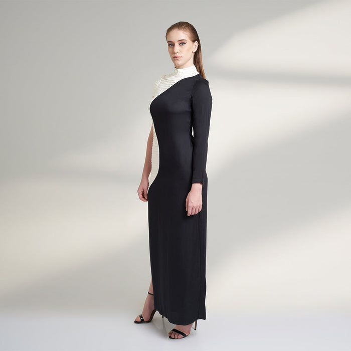 A medium size model wearing a black and white half and half dress made from organic lotus stem fabric. This sustainable vegan dress is a long floor length dress with one side pleated in white and one side plain black with a thigh high side slit striking a side pose.